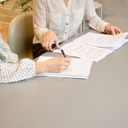 two women sitting at a table with papers | ask2axcel